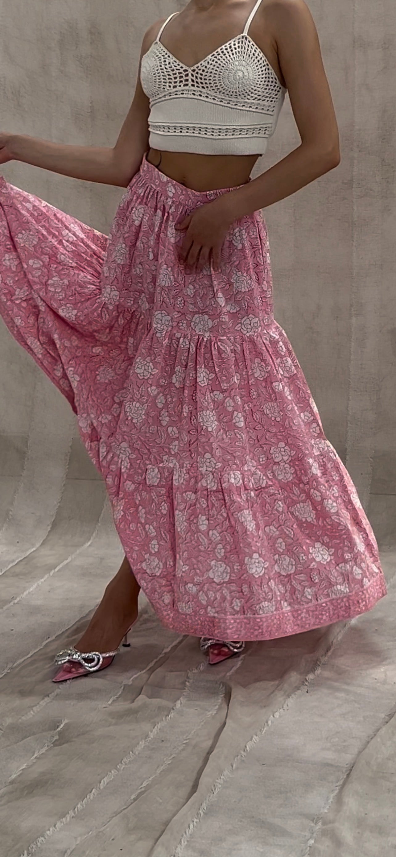 Woman wearing a white lace top and pink floral skirt on a neutral background